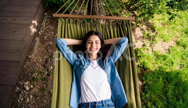 ハンモックに揺られてゆったり過ごす女性 ハンモックチェア,アウトドア,キャンパーの写真素材