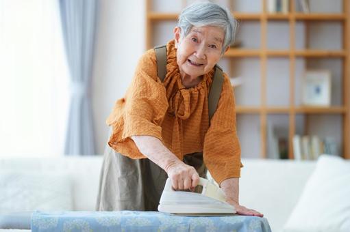 右手でアイロンを持つショートヘアの高齢女性 女性,アイロン,アイロン台の写真素材