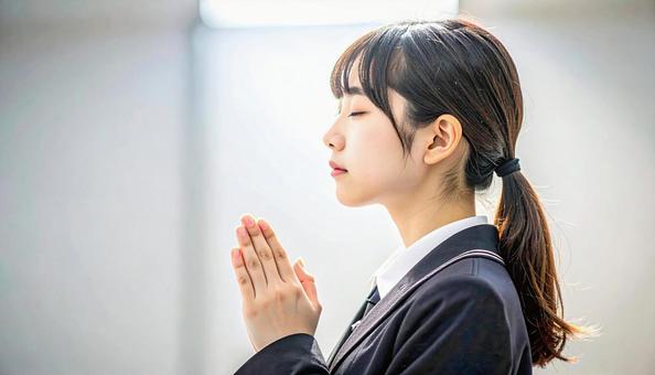 手を合わせて受験合格を祈る制服の女子高生の写真