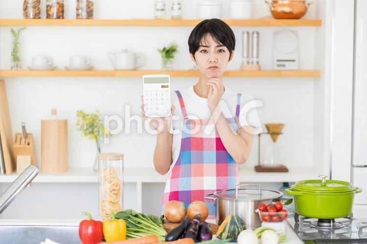 電卓を持って悩む主婦。 電卓を持って悩む主婦。 主婦,キッチン,悩みの写真素材