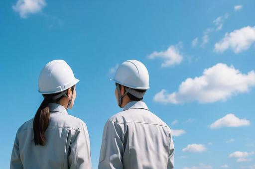 青空を見上げる作業服とヘルメットの男女 青空を見上げる作業服とヘルメットの男女の写真