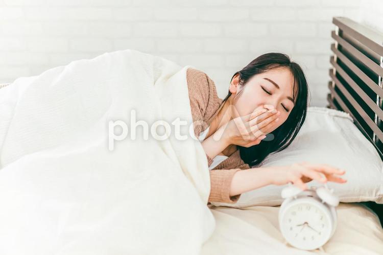 ベッドルームで目覚まし時計を止める女性 眠い,あくび,不眠症の写真素材