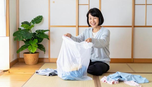 不要の衣類をゴミ袋に捨てるシニア女性 不要の衣類をゴミ袋に捨てるシニア女性の写真