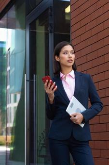 オフィスビルのエントランスでタブレットとスマートフォンを持って立つビジネスウーマン ビジネスウーマン,ビジネス,女性の写真素材