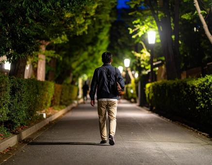 街灯の下を歩く男性の後ろ姿の写真