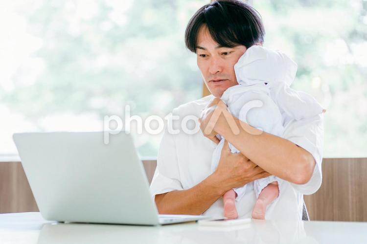 赤ちゃんを抱きながら仕事する男性 テレワーク,育児,リモートワークの写真素材