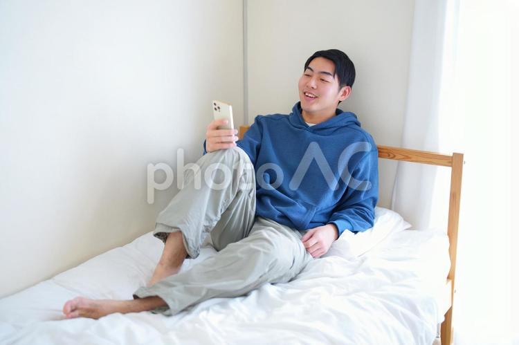 ベッドでくつろぎながらスマートフォンを見ている男性 引っ越し,一人暮らし,男性の写真素材