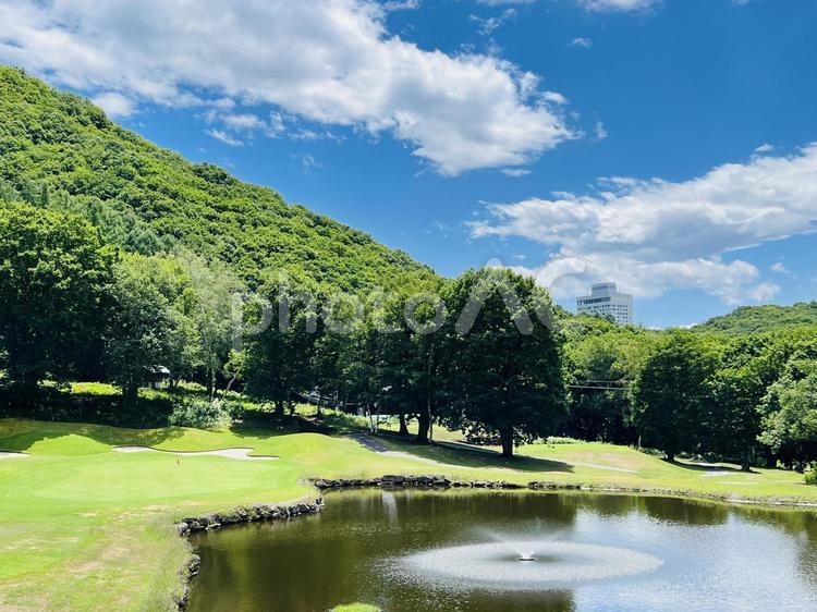 噴水のある池と山々のゴルフコース風景 ゴルフ場,ゴルフコース,フェアウェイの写真素材