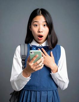 スマートフォンを見て驚く女子学生 スマートフォンを見て驚く女子学生の写真