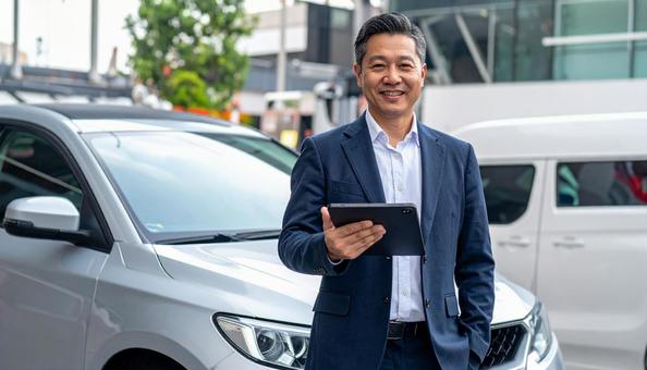 車の前に立つディーラーの日本人男性 車の前に立つディーラーの日本人男性の写真