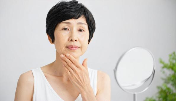 ほうれい線を気にしてほほを触る中年の女性の写真