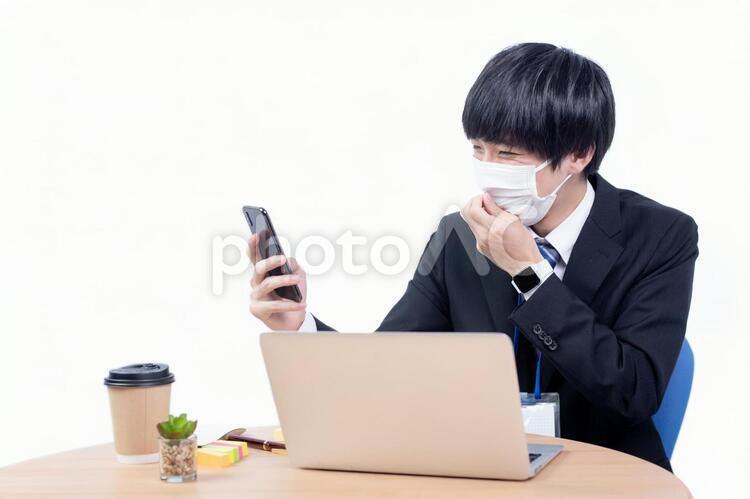 スマホを操作しながらマスクに手をかける若い日本人サラリーマン マスク,健康,ヘルスケアの写真素材