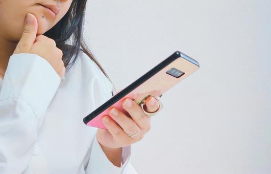 スマホを見て悩んでいる女性 スマホを見て悩んでいる女性 悩む,スマホ,スマートフォンの写真素材