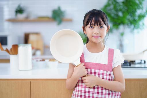 フライパンを手に笑顔を見せるエプロン姿の女の子 女の子,フライパン,持つの写真素材