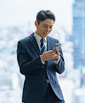 高層ビルで携帯を持つビジネスマン 高層ビルで携帯を持つビジネスマン ビジネスマン,男性,スーツの写真素材