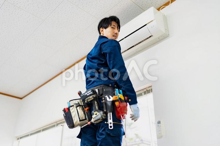 エアコンの前で立つ電気工事作業員 ビジネス,ビジネスマン,男の写真素材