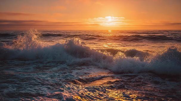 砕け散る波と燃えるような朝焼けの海の写真
