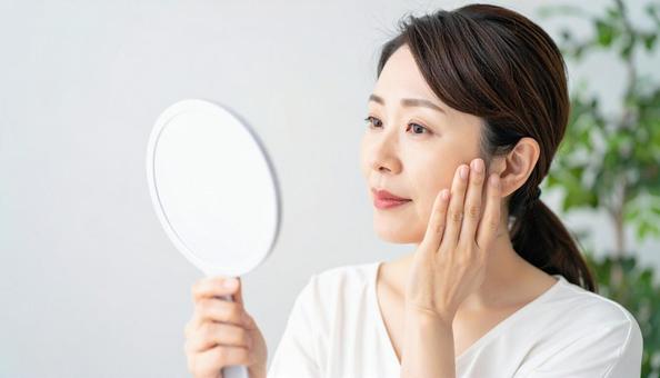 ほうれい線を気にしてほほを触る中年の女性の写真