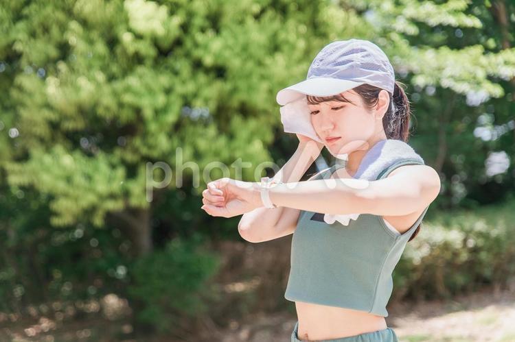 公園で腕時計を見ながら運動をする女性 スポーツウォッチ,疲労,熱中症対策の写真素材