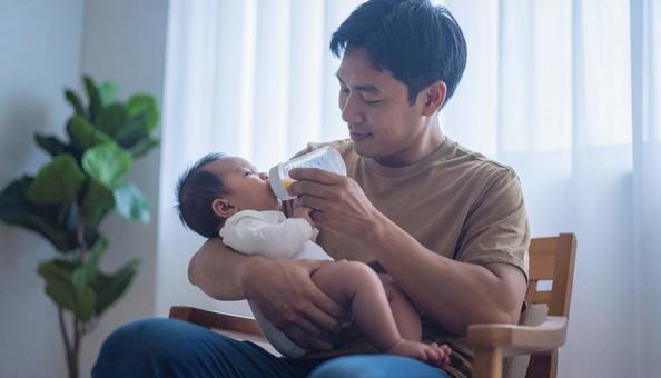 椅子に座り赤ちゃんに哺乳瓶で授乳する父親 椅子に座り赤ちゃんに哺乳瓶で授乳する父親の写真