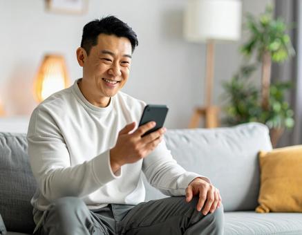 自宅でスマホを操作する男性 自宅でスマホを操作する男性の写真