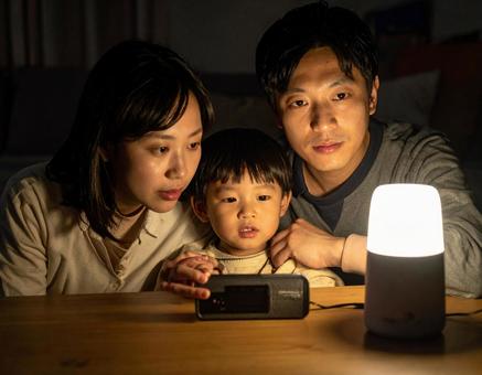 災害で停電の夜にラジオで情報収集する家族 災害で停電の夜にラジオで情報収集する家族の写真