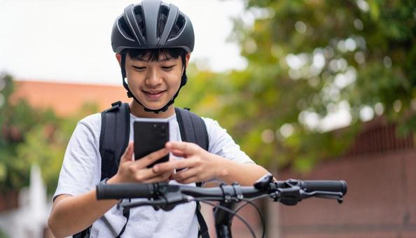 自転車を止めてスマホを見る男の子 自転車を止めてスマホを見る男の子の写真