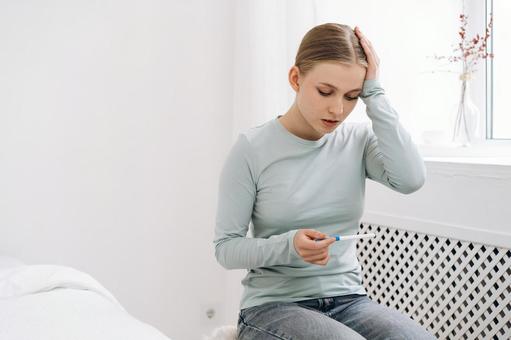 窓際に座り妊娠検査薬を見て悩む女性 窓際に座り妊娠検査薬を見て悩む女性 女性,妊娠検査薬,持つの写真素材