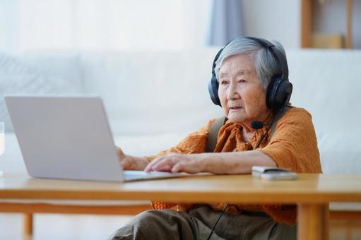 パソコンを見るヘッドセットの高齢女性 女性,ノートパソコン,座るの写真素材