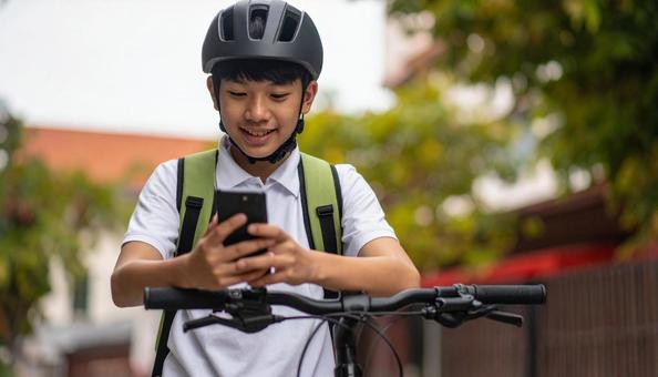 自転車を止めてスマホを見る男の子 自転車を止めてスマホを見る男の子の写真