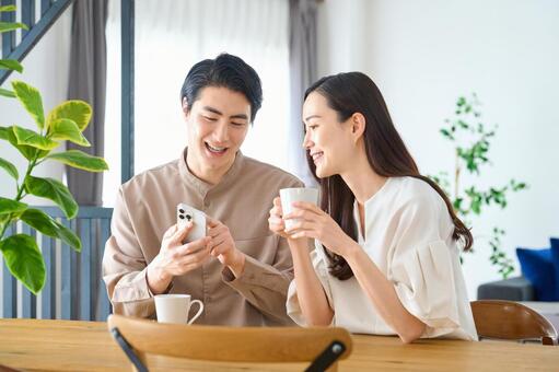 スマホを見ながら談笑するリビングの夫婦