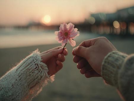 ビーチで交わされる花と手の写真