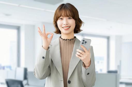 スマホを持ってOKポーズをする笑顔の女性 女性,ok,スマホの写真素材