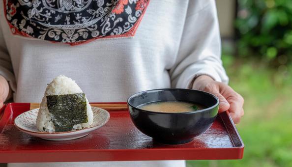 お盆に乗ったおにぎりと味噌汁を持つ女性 お盆に乗ったおにぎりと味噌汁を持つ女性の写真