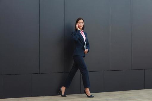 オフィスビルの外で歩きながらスマートフォンで電話しているビジネスウーマン ビジネスウーマン,ビジネス,女性の写真素材