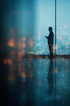 夜景を見ながらタブレットを使う男性 夜景を見ながらタブレットを使う男性の写真