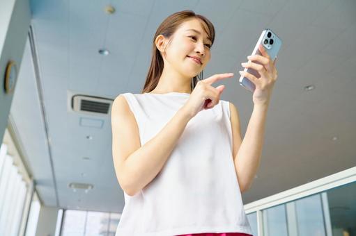 ジムでスマホを操作する女性 スマホ,女性,スポーツジムの写真素材