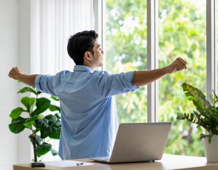 窓辺で伸びをする若手社員 窓辺で伸びをする若手社員の写真