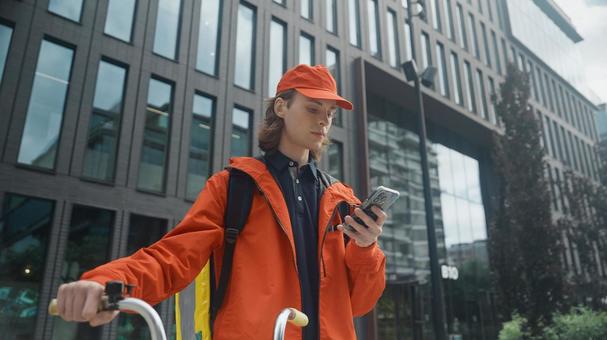 街なかでスマートフォンを見ている自転車のフードデリバリーの男性 配達,フードデリバリー,デリバリーの写真素材