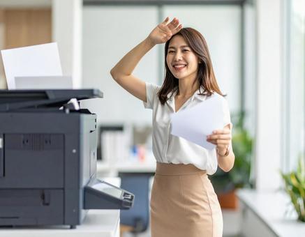 オフィスで汗を拭きながら笑顔を見せる女性 オフィスで汗を拭きながら笑顔を見せる女性の写真