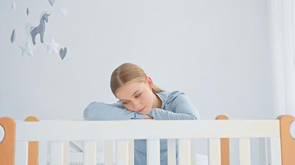 疲れた表情でベビーベッドを覗く女性 疲れた表情でベビーベッドを覗く女性の写真