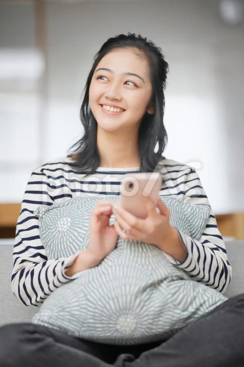 スマホを持ち座り横を見る女性 女性,スマホ,振り向くの写真素材