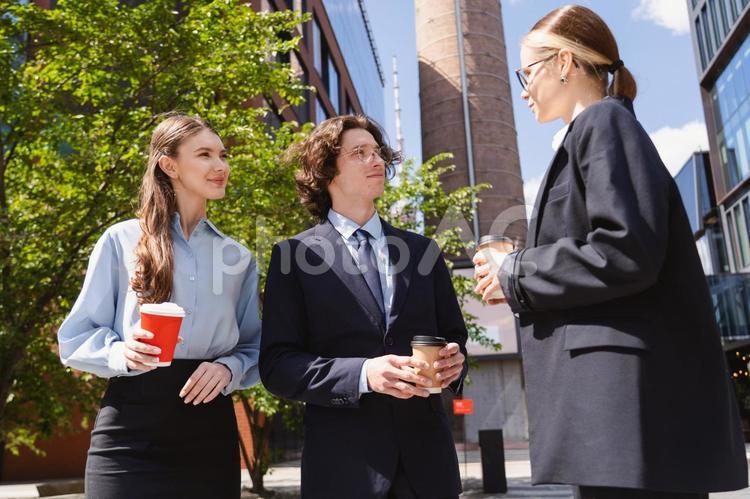 オフィスビルの前でコーヒーを持って立ち話する男女 ビジネス,グループ,ビジネスマンの写真素材