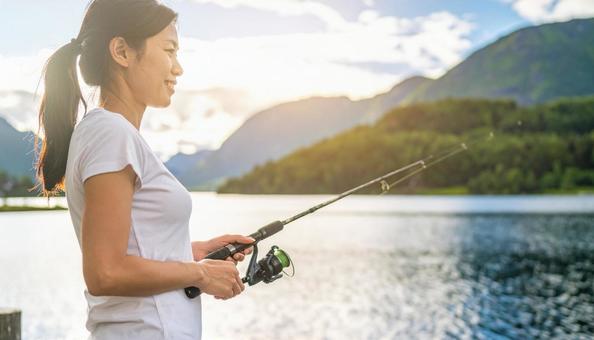 湖で回転する釣り竿で釣りをする若い女性 湖で回転する釣り竿で釣りをする若い女性の写真