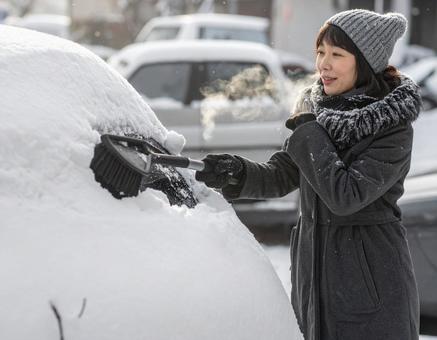 冬に車に積もった雪を雪下ろしする女性 冬に車に積もった雪を雪下ろしする女性の写真
