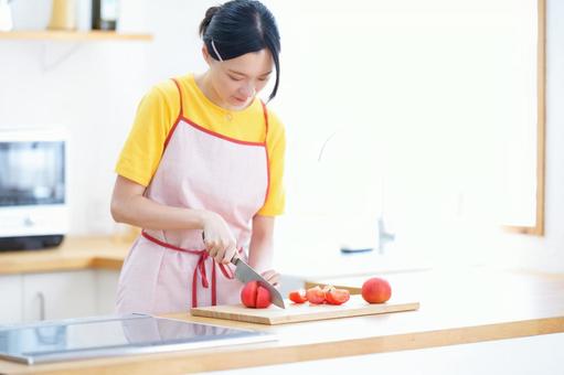 包丁でトマトを切っているエプロンの女性の写真