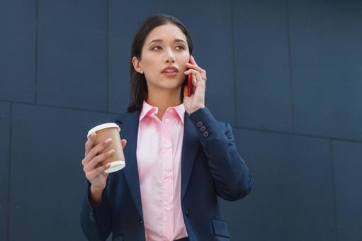 オフィスビルの外でコーヒー片手に電話しているアジア人女性 ビジネスウーマン,ビジネス,女性の写真素材