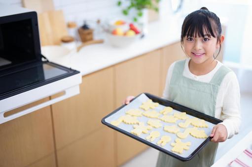 オーブンの前で天板を掲げるエプロン姿の少女 女の子,日本人,クッキーの写真素材