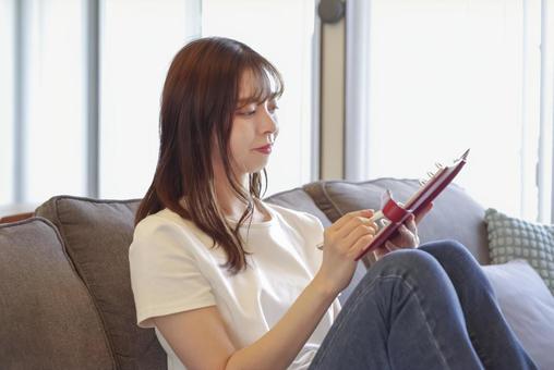 リビングで手帳の予定を確認する女性 ノート,手帳,スケジュール帳の写真素材