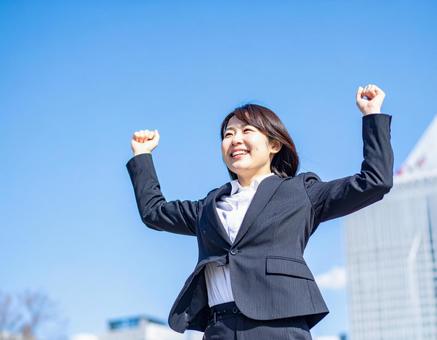 青空の下ガッツポーズする女性社員 青空の下ガッツポーズする女性社員の写真